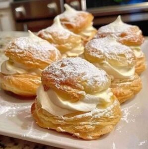 Delicious cream puffs filled with fluffy whipped cream, topped with a light dusting of powdered sugar, served on a white plate