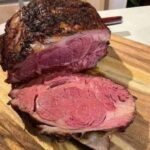 This image showcases a beautifully cooked Prime Rib Roast with a perfectly browned crust on the outside and a juicy, pink center that indicates medium-rare doneness. The marbling throughout the meat ensures exceptional tenderness and flavor, while the carving reveals a clean, even slice. This roast is likely prepared using the reverse sear method, achieving both a crispy crust and consistent doneness. Served on a wooden cutting board, it's ready to be the centerpiece of a hearty and elegant meal.